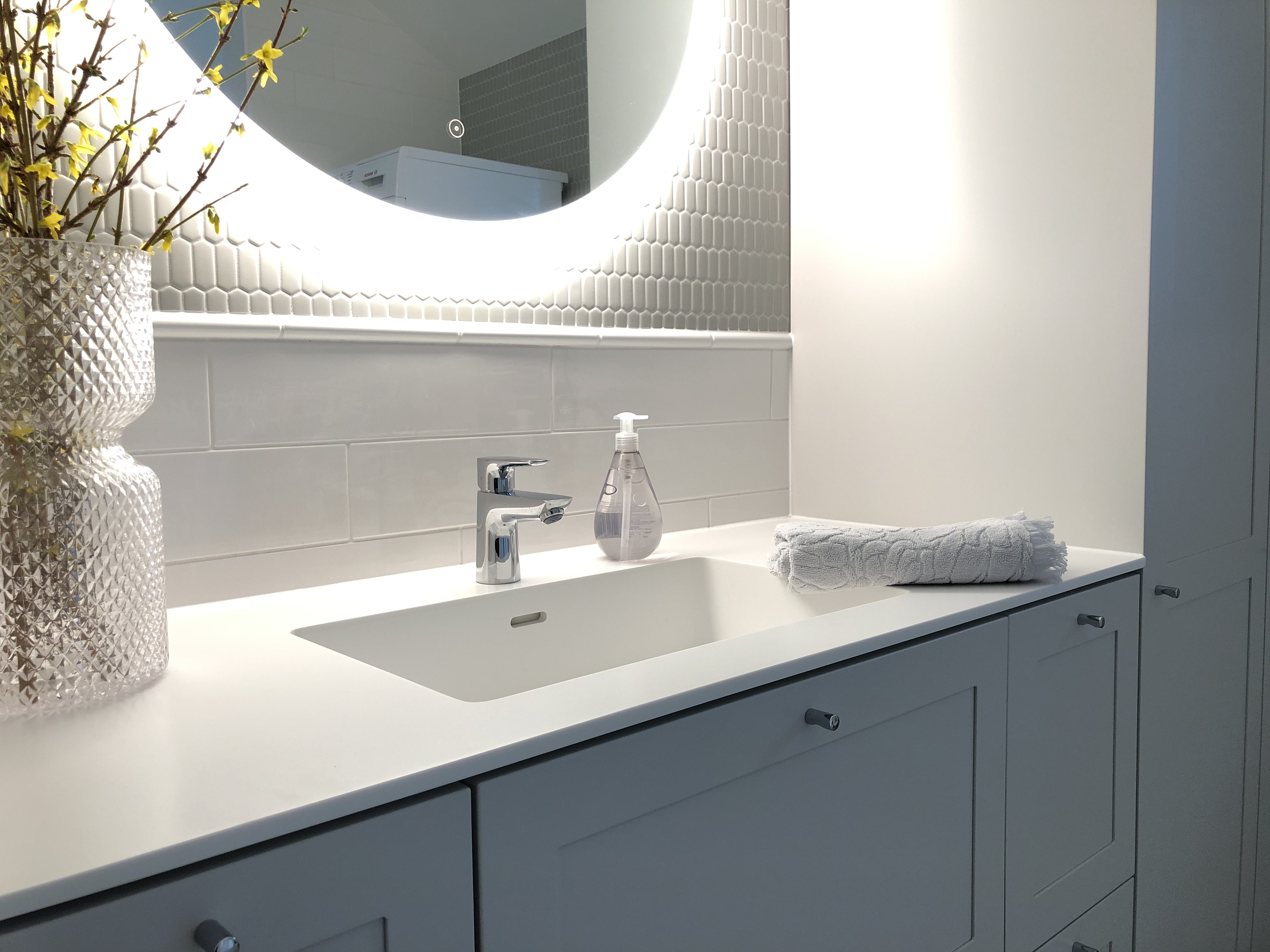 Referenssi kylpyhuoneremontista - vaalea, mosaiikkia, valkoiset suorakaiteen muotoiset laatat ja tiililadonta kylpyhuoneen seinällä.